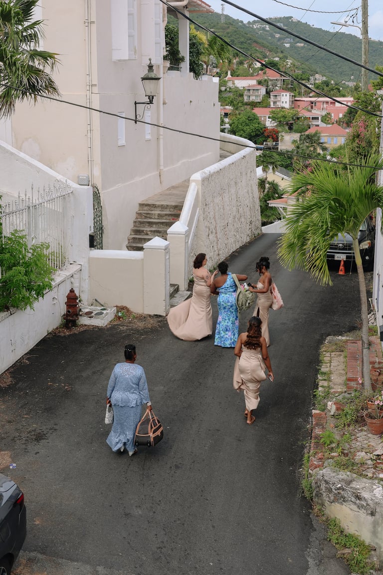 Group of people walking on a narrow street in a hillside Caribbean neighborhood with white and colorful buildings