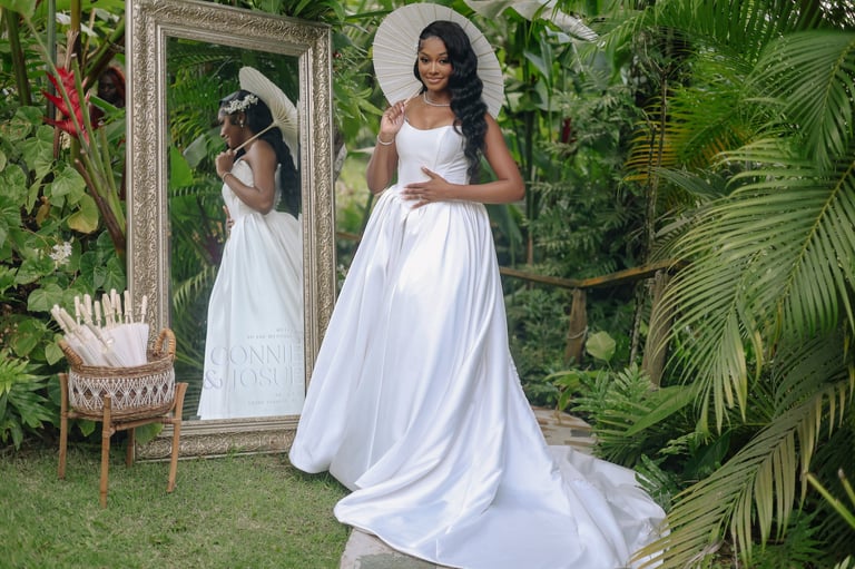 Woman in white wedding gown posing with decorative mirror in lush garden setting surrounded by green plants
