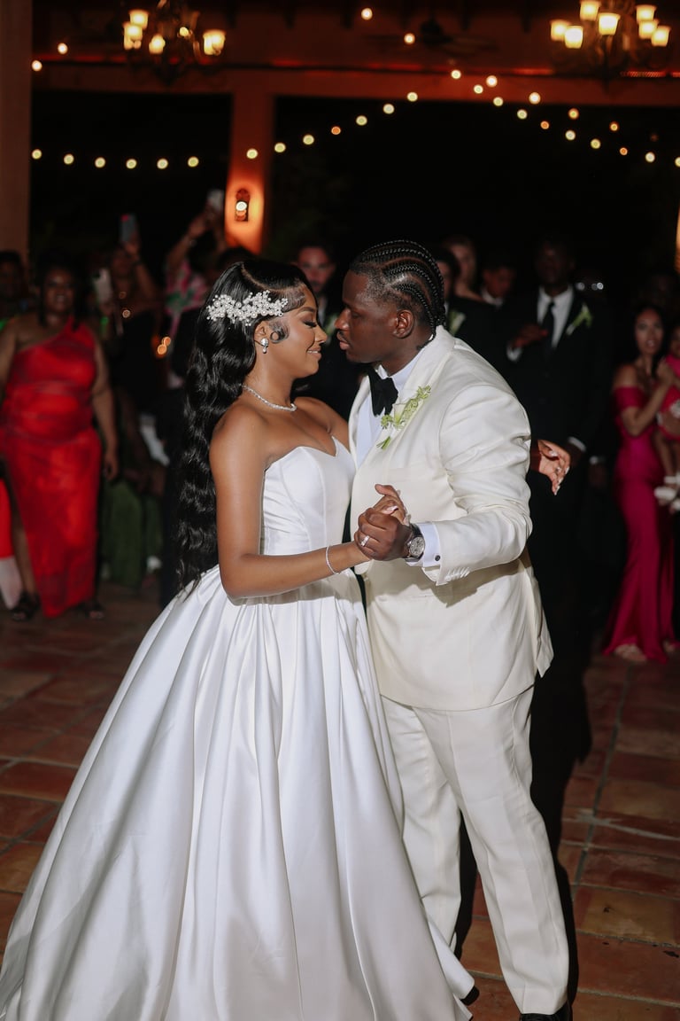 Bride and groom share first dance at wedding reception with string lights and guests in background