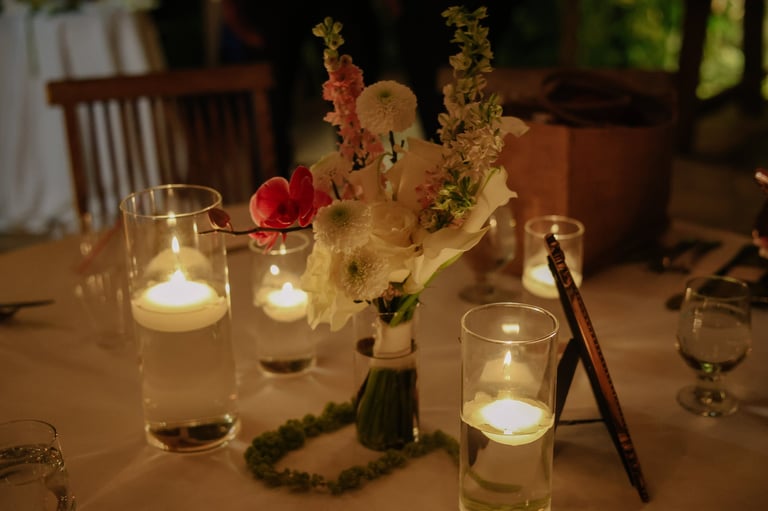 Elegant table setting with white flowers, red rose, lit candles in glass holders, and dining utensils on a wooden table