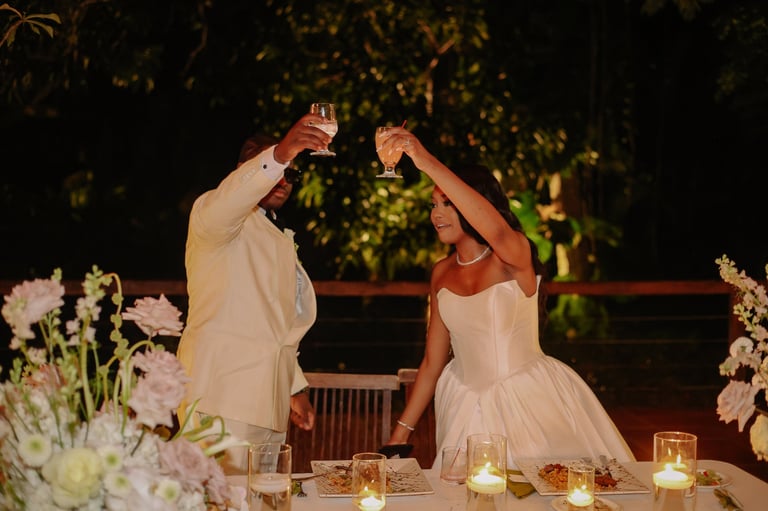 Bride and groom clinking champagne glasses during nighttime wedding reception with candlelit tables and floral arrangements
