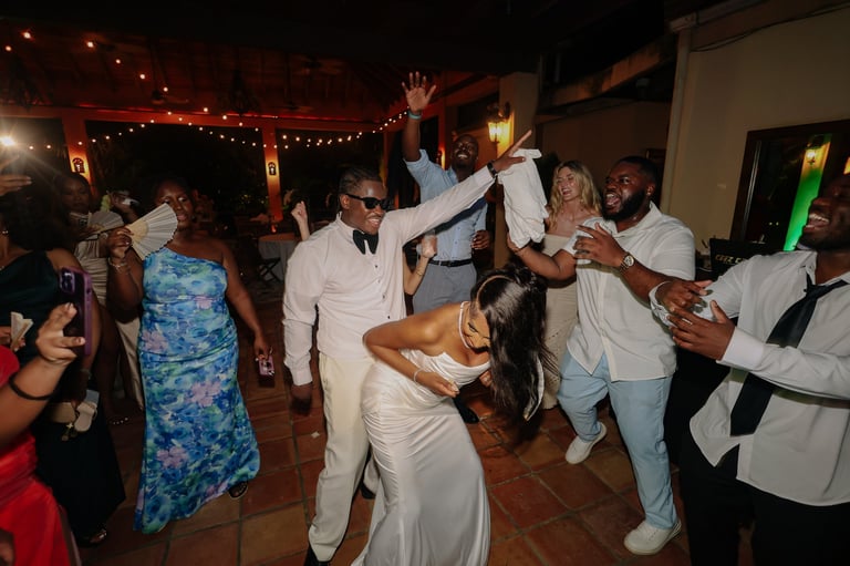 Group of people in white and colorful clothing dancing and celebrating at an indoor event with decorative string lights overhead