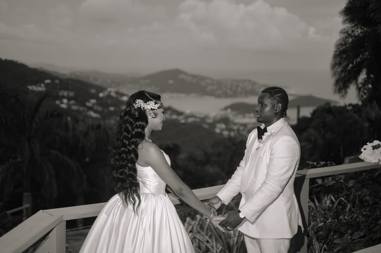 Bride and groom holding hands on a terrace overlooking a scenic lake and mountainous landscape in black and white