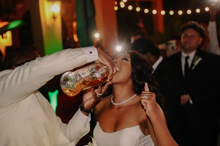 Woman in white dress drinking from glass at festive party with string lights and guests in background