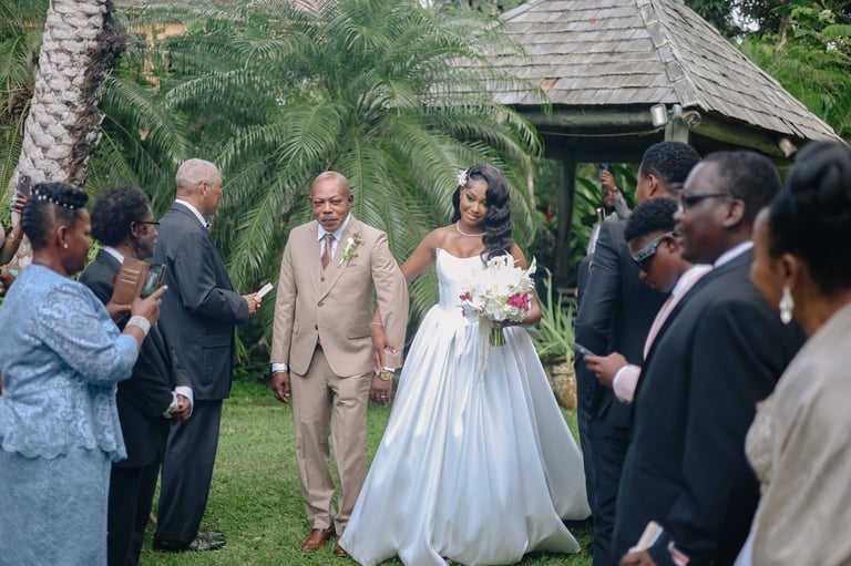 Bride and groom walking down garden aisle surrounded by formally dressed wedding guests in tropical setting
