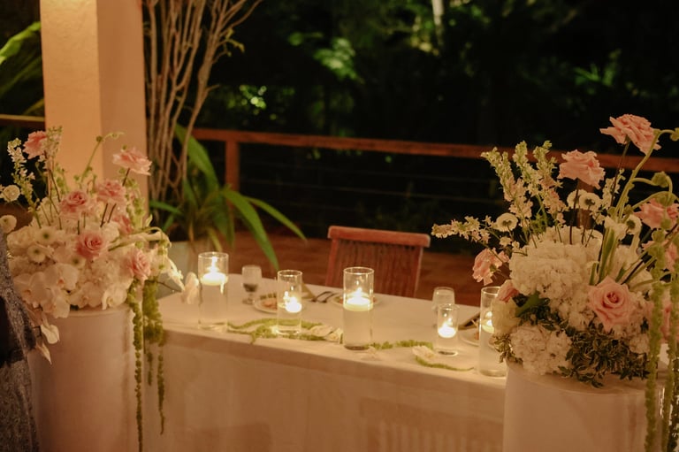 Outdoor evening reception table decorated with floral arrangements and candles under warm lighting