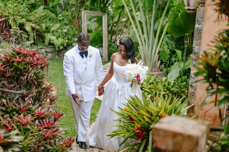 Bride and groom walking hand-in-hand through a lush garden with tropical plants during their wedding ceremony