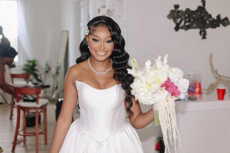 Woman in white wedding dress holding white and pink floral bouquet, wearing pearl necklace and long dark wavy hair