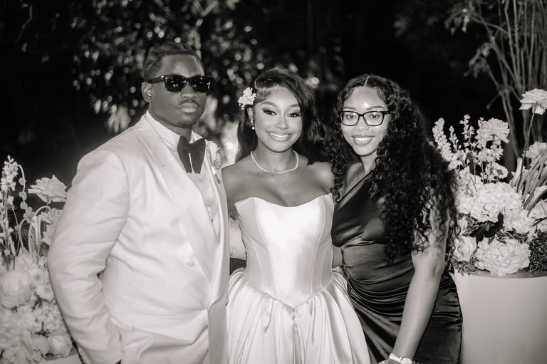 Three people dressed formally at an elegant event, posing together in front of floral decorations in a black and white photo
