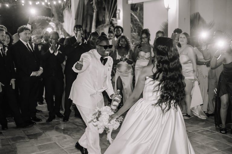 Bride and groom dancing at wedding reception surrounded by guests in formal attire, black and white photograph