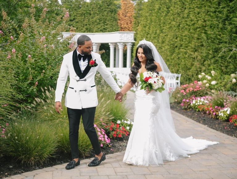 Bride and groom walking hand-in-hand in a formal garden setting surrounded by colorful flowers and greenery