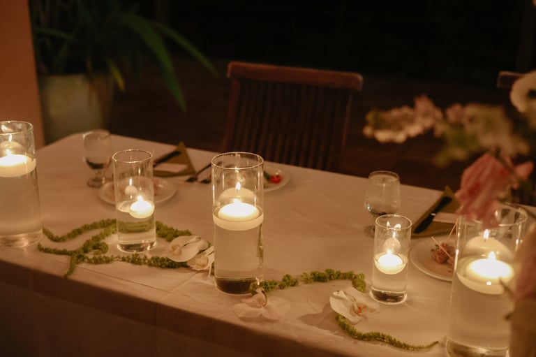 Elegant outdoor dinner table decorated with lit candles in glass holders and greenery garland at night