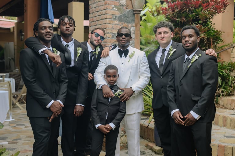 Group of men and a young boy in formal attire posing together outdoors at what appears to be a wedding celebration